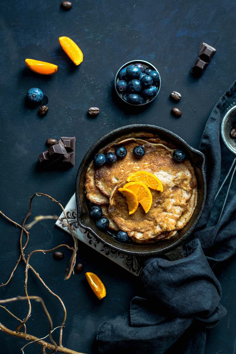 food photography pancake with orange and blueberries beside scattered chocolate and coffee beans food styling